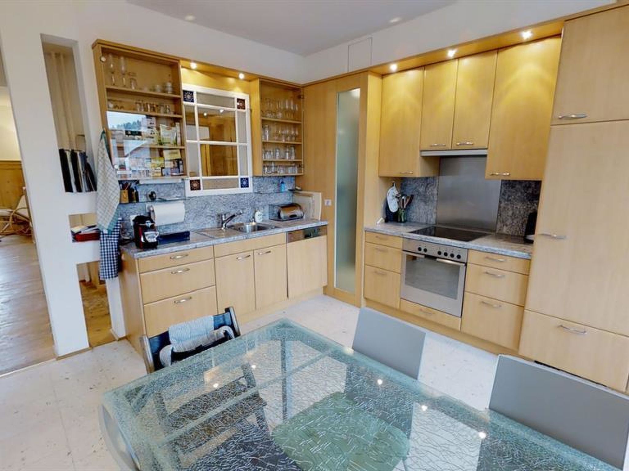 Una cocina moderna con armarios de madera, una estufa de acero inoxidable y una mesa de comedor de vidrio.