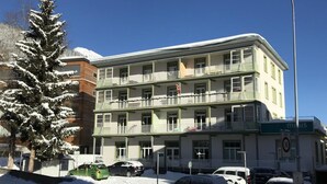 Um edifício com várias andares, varandas, carros estacionados e uma árvore coberta de neve.