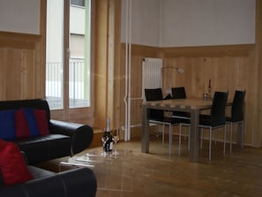 A room with a wooden floor, a black leather sofa with red and blue cushions, a dining table with four chairs, and a radiator. - Rialto 05 Appartement/Fewo, Dusche oder Bad, WC 4½-Zimmerwohnung by Interhome (Davos)