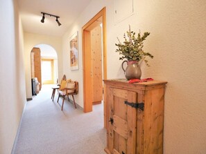 Un pasillo con un armario de madera, una silla y un jarrón con flores.