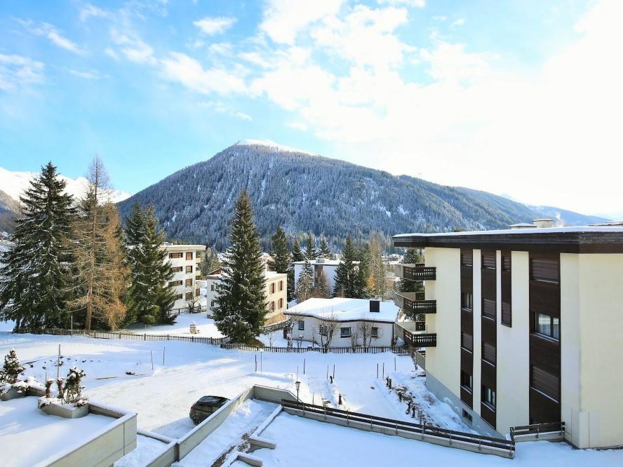 Ett snötäckt landskap med byggnader, träd och ett berg i bakgrunden.