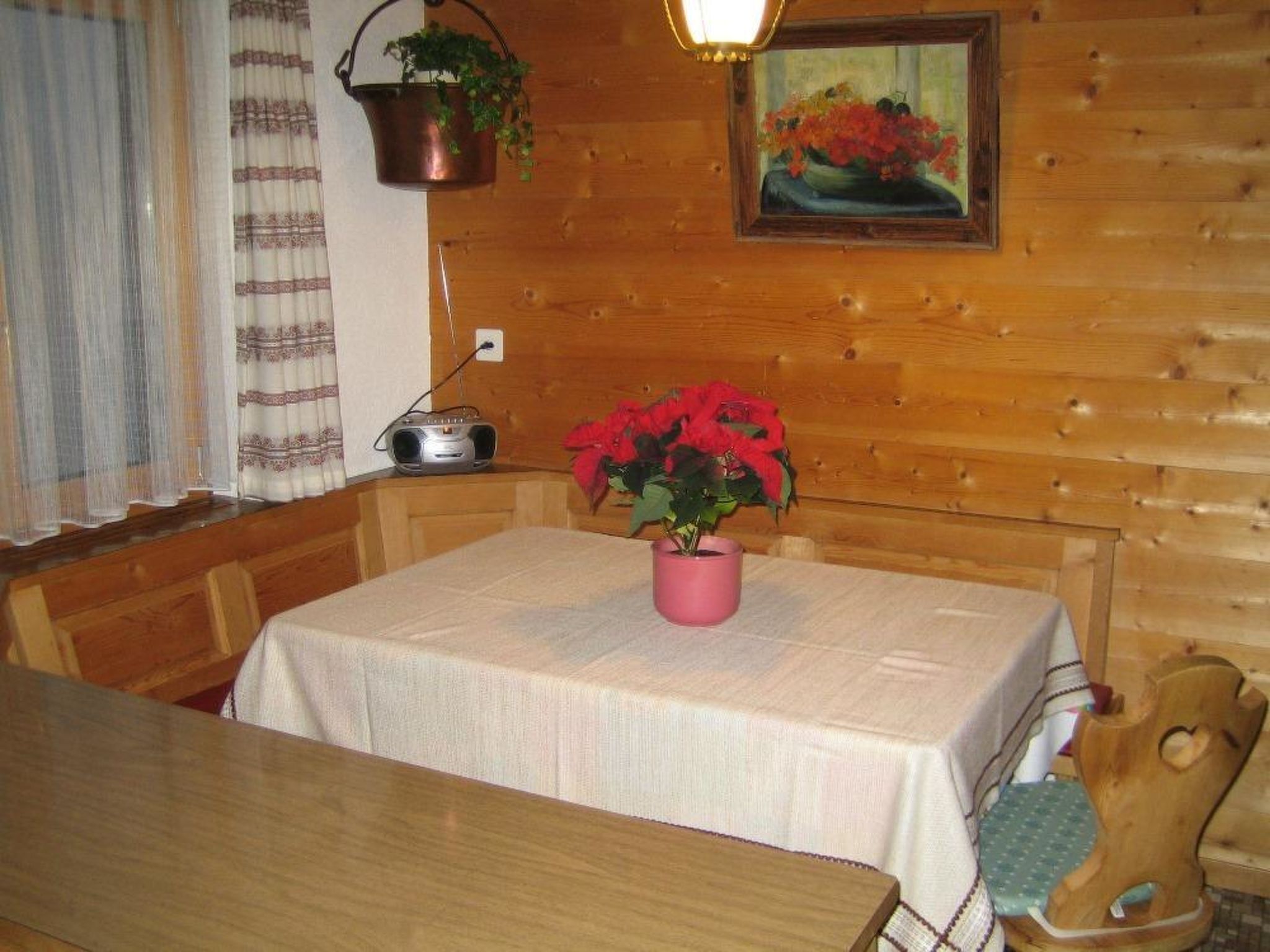 A wooden interior with a table, chairs, a radio, and a potted plant.