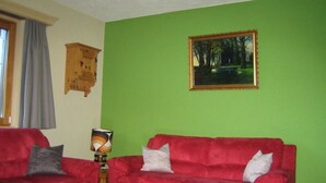 Un salon avec deux canapés rouges, une table basse en bois, un mur vert et un tableau encadré.