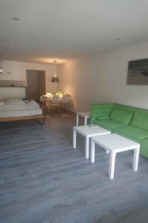 A modern living room with a green sofa, white coffee tables, a dining area with a table and chairs, and a bed with white bedding. - Appartmenthaus Lenza 504 Appartement/Fewo, Dusche oder Bad, WC 1½-Zimmerwohnung by Interhome (Davos)