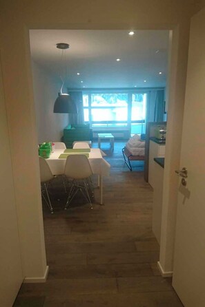 Un estrecho pasillo que conduce a un comedor con una mesa y sillas, una ventana con vistas y una puerta a la derecha.
