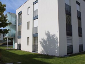 Un edificio moderno con varias ventanas y balcones, rodeado por un césped bien cuidado.