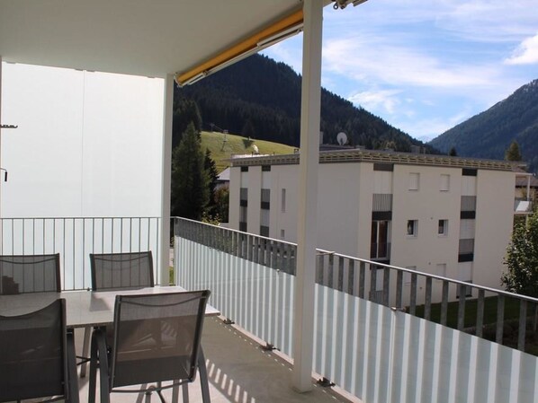 Ein Balkon mit Tisch und Stühlen, mit Blick auf ein Gebäude und Berge.