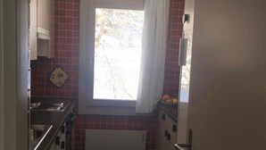 Et smalt køkken med et vindue, en radiator og en dør.