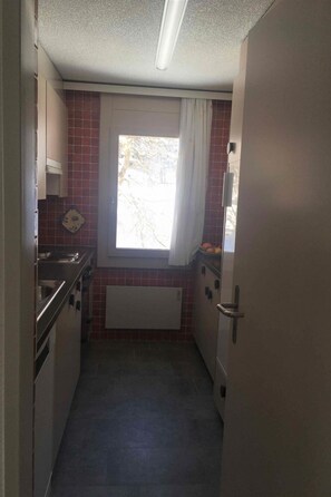 Eine schmale Küche mit Fenster, Heizkörper und Tür.