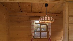 Interno di una baita in legno con un tavolo a scacchi, una sedia, una panca e una finestra con tende.