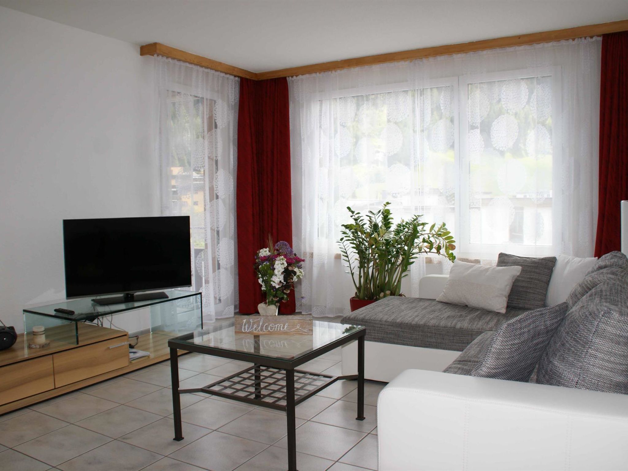 Ein Wohnzimmer mit Fernseher, Glastisch, Sofa und einer Willkommensschild.