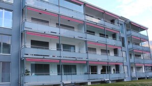 Un edificio residenziale a più piani con balconi, tetto piano e un'area verde davanti.