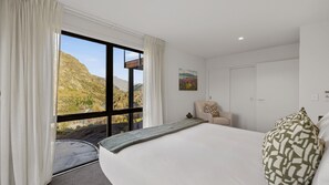 A hotel room with a large bed, a chair, a painting, and a view of a mountainous landscape. - Powder Ridge Alpine Retreat (Queenstown)