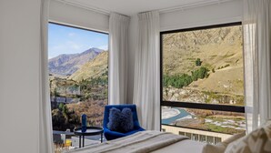 Habitación de hotel con un ventanal amplio que ofrece vistas a la montaña, una silla azul y una pequeña mesa con una botella.