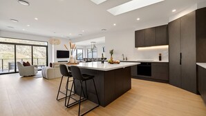 Cocina moderna con una isla central, taburetes de bar, zona de comedor con sofá y un amplio ventanal con vistas.