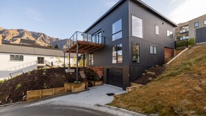Una casa moderna de dos pisos con garaje, un espacio exterior cubierto y vistas a montañas al fondo.