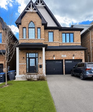 A two-story house with a brick facade, a black front door, and two garage doors. - Luxurious Detached Five-Bedroom House in Mississauga. (Mississauga)