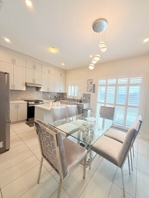 A modern kitchen with white cabinets, a glass dining table, and a stainless steel refrigerator. - Luxurious Detached Five-Bedroom House in Mississauga. (Mississauga)