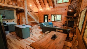 A cabin interior with a wooden dining area, a sofa, a fireplace, and a kitchen with a stove. - Knotty Summit| Hocking Hills, Theater, Hot Tub (Logan)