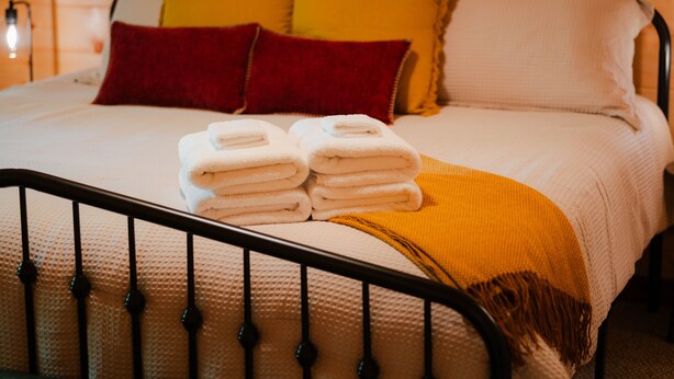 A bed with a metal frame, white bedding, and a yellow throw blanket. - Knotty Summit| Hocking Hills, Theater, Hot Tub (Logan)