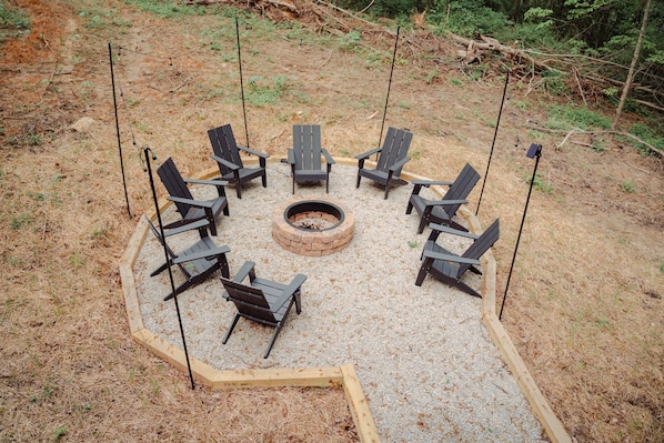 A circular seating arrangement around a central fire pit with chairs and a wooden deck.