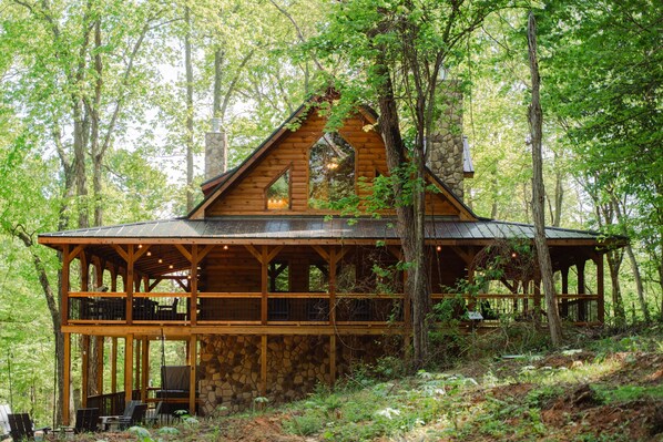 A wooden cabin with a stone foundation, surrounded by trees.