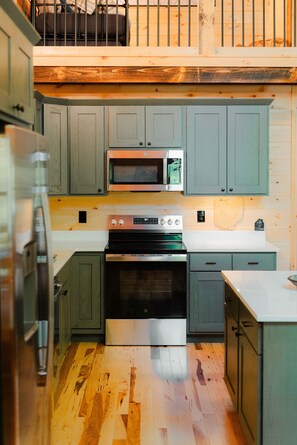 A compact kitchen with wooden cabinets, a microwave, a stove, and a refrigerator.