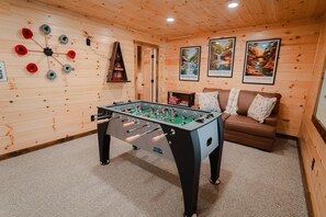 A cozy room with a foosball table, a brown sofa, and two framed pictures on the wall.
