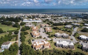 Luchtbeeld van een kustgebied met woonhuizen, wegen en een strand in de verte.