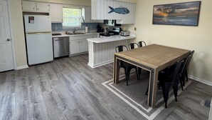Una cocina con armarios blancos, una mesa de comedor de madera y un cuadro en la pared.