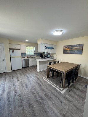Een keuken met witte kastjes, een houten eettafel en een schilderij aan de muur.