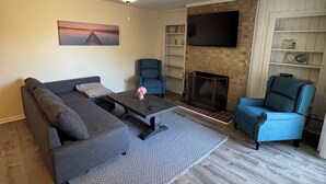 Una sala de estar con sofá, sillones, una mesa de centro, chimenea, televisor y ventilador de techo.