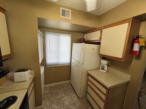Una cocina compacta con refrigerador, tostadora, cafetera y una ventana con persianas.