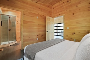 A wooden-paneled bedroom with a bed, a glass shower enclosure, and a door leading to a balcony.