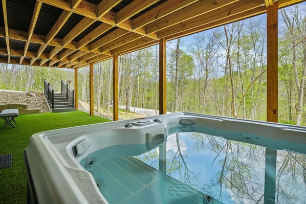 A hot tub with a wooden deck and large windows overlooking a forest.