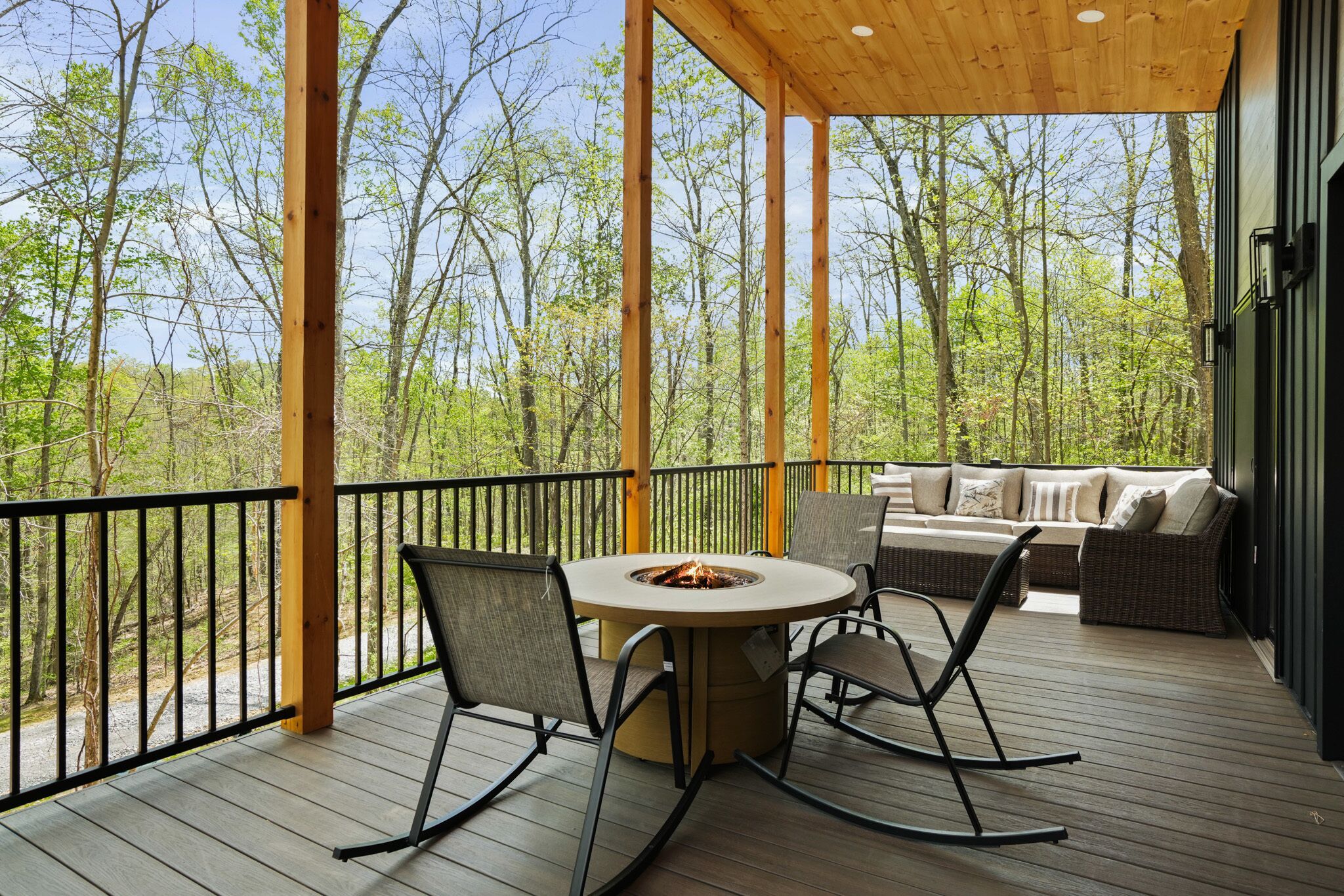 A wooden deck with a round table and chairs, a fire pit, and a sofa with cushions.