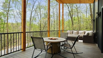 A wooden deck with a round table and chairs, a fire pit, and a sofa with cushions.