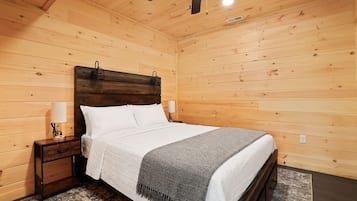 A wooden-paneled bedroom with a bed, nightstands, lamps, and a ceiling fan.