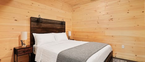A wooden-paneled bedroom with a bed, nightstands, lamps, and a ceiling fan.