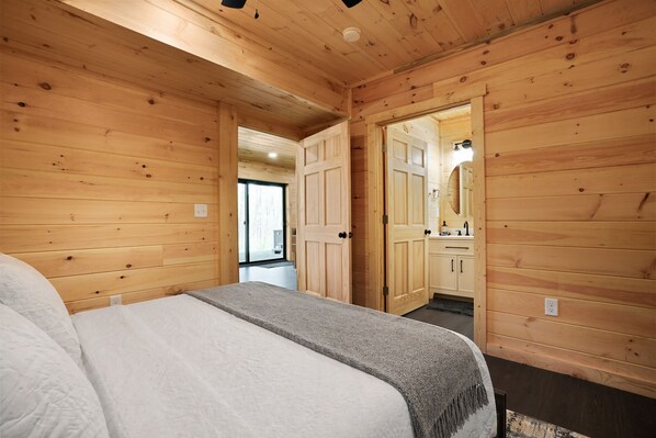 A wooden-paneled bedroom with a bed, a bench, and a door leading to a bathroom.