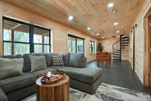 A wooden interior with a sectional sofa, a wooden coffee table, a spiral staircase, and large windows.
