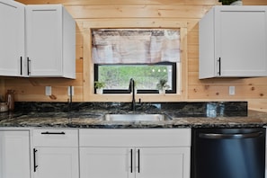 A kitchen with white cabinets, a granite countertop, a black faucet, and a window with a view of greenery.