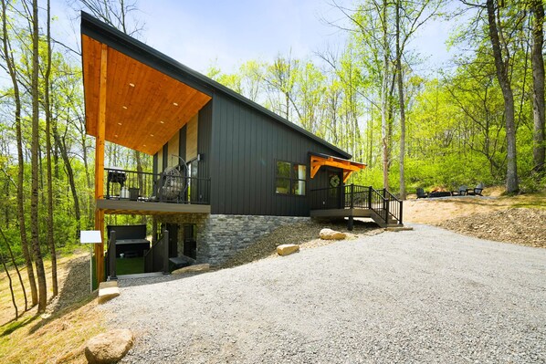 A modern two-story cabin with a stone foundation, large windows, and a wooden deck.
