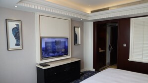 Habitación de hotel con cama, televisor sobre un soporte, puerta y pared decorada con cuadros.