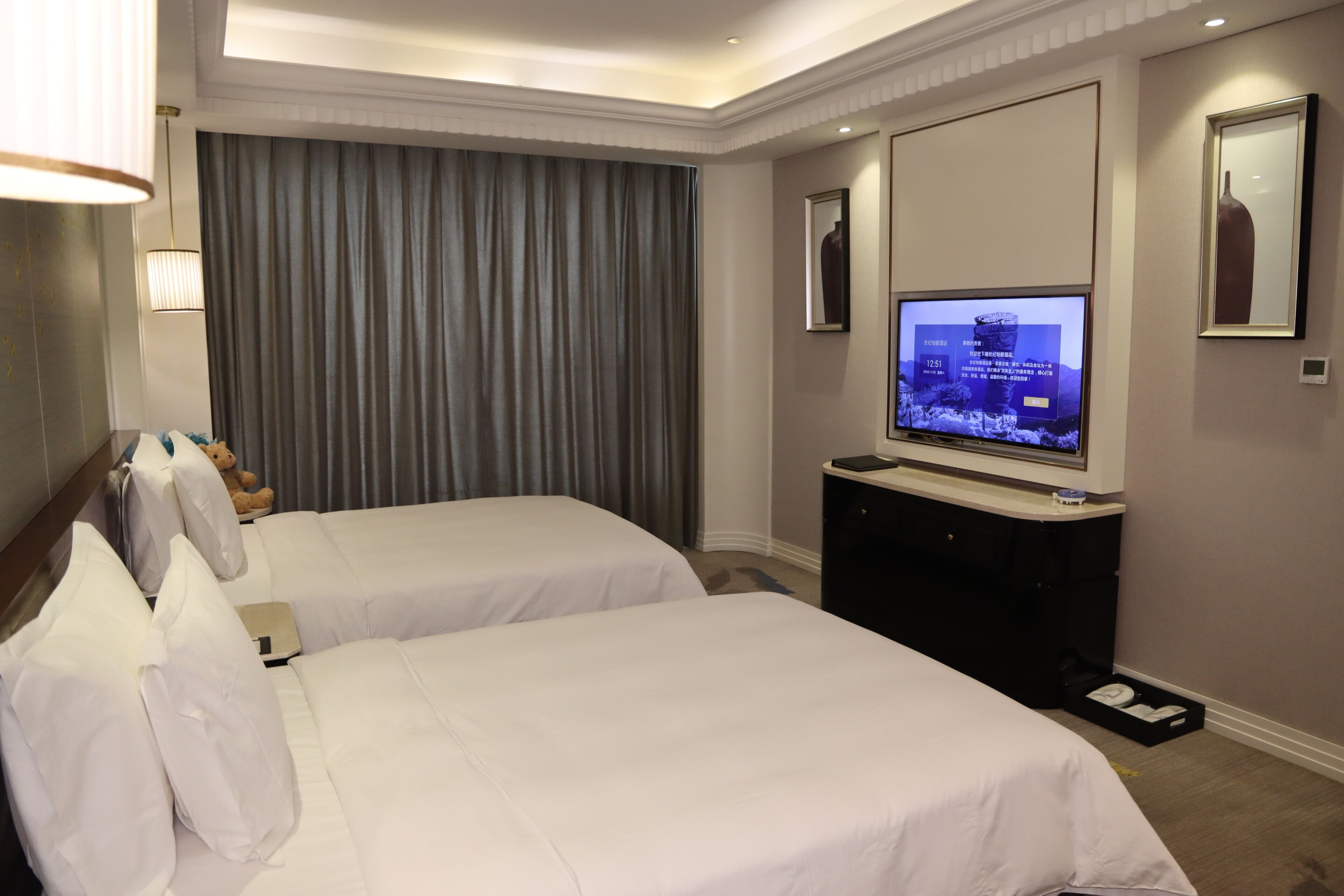 Una habitación de hotel con dos camas, televisión, escritorio y un ventanal con cortinas.