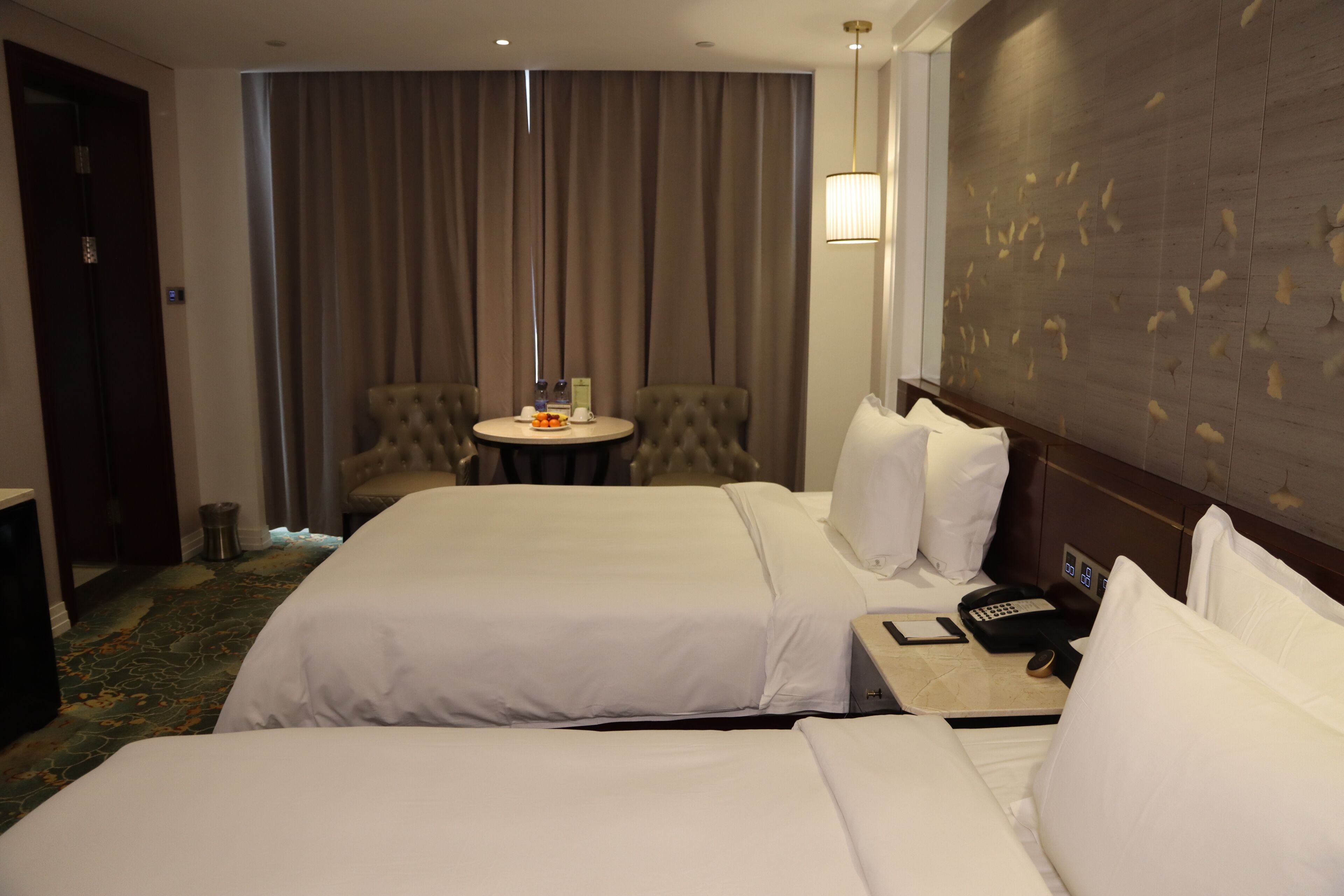 Une chambre d’hôtel avec deux lits, une petite table ronde avec une télécommande, une chaise et un luminaire fixé au mur.