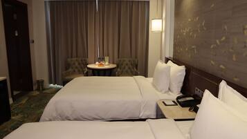 Une chambre d’hôtel avec deux lits, une petite table ronde avec une télécommande, une chaise et un luminaire fixé au mur.