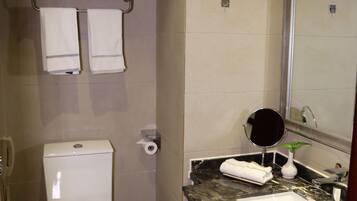 Un baño con inodoro, lavamanos, espejo y toallero.