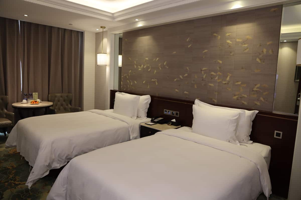 A hotel room with two beds, a round table with a chair, a wall-mounted phone, and a mirror.