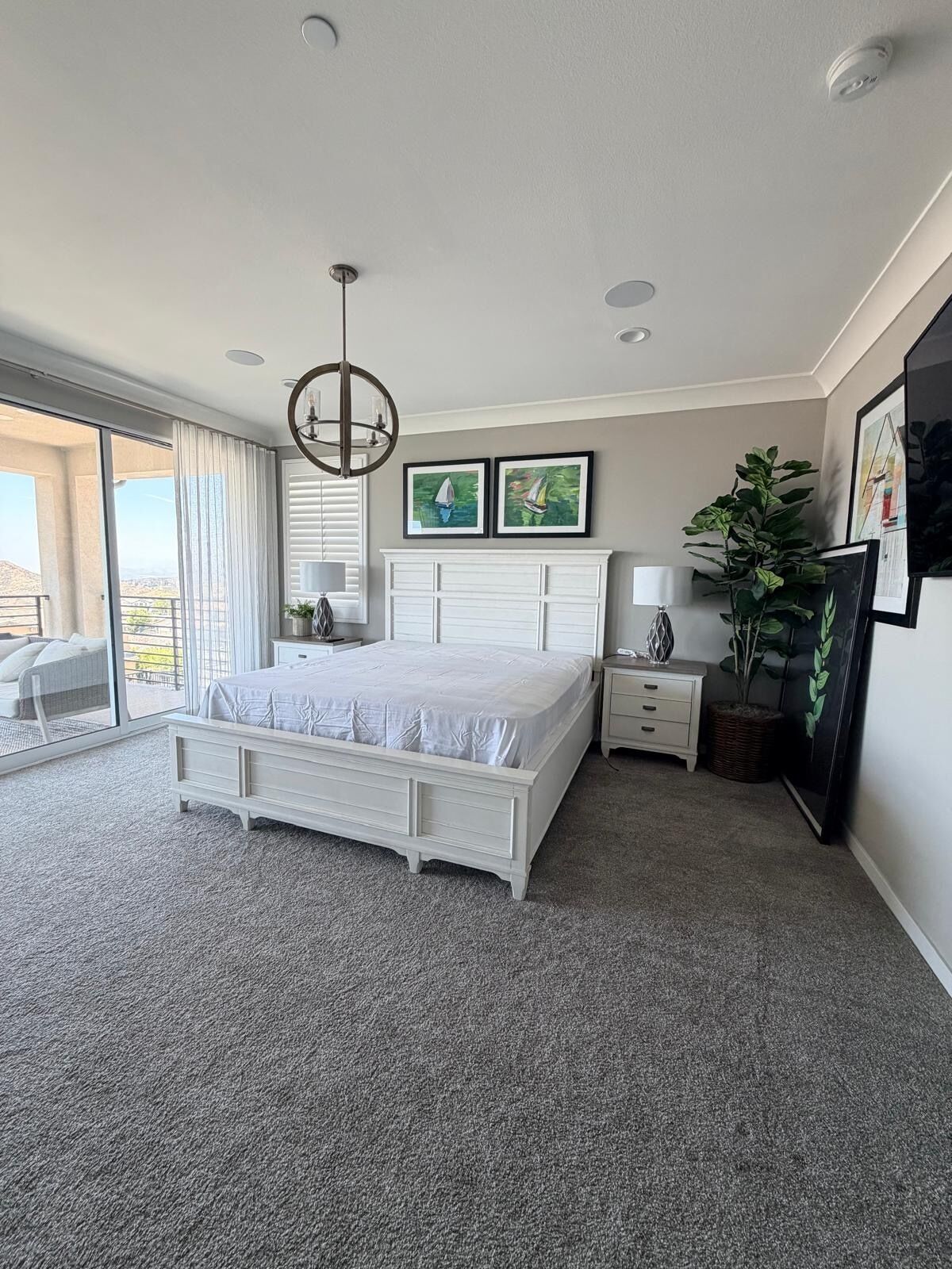 A bedroom with a large bed, a bedside table, a nightstand, a potted plant, and a view of the outdoors.
